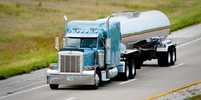 A large tanker truck with blue cab travels on highway