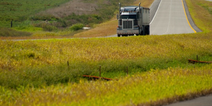 Dark semi truck drives down rural highway green median in foreground